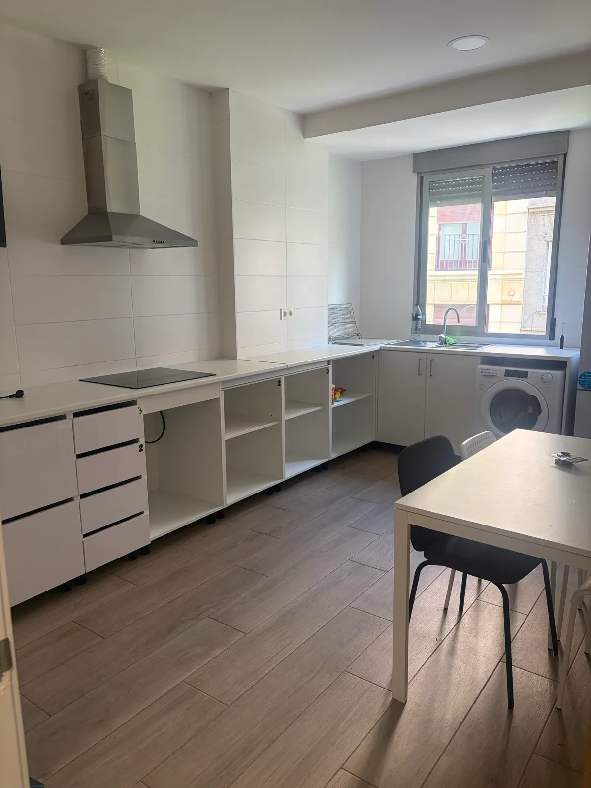 Cocina común de Greenhome Lepanto con vitrocerámica, campana extractora, lavadora y mesa de comedor